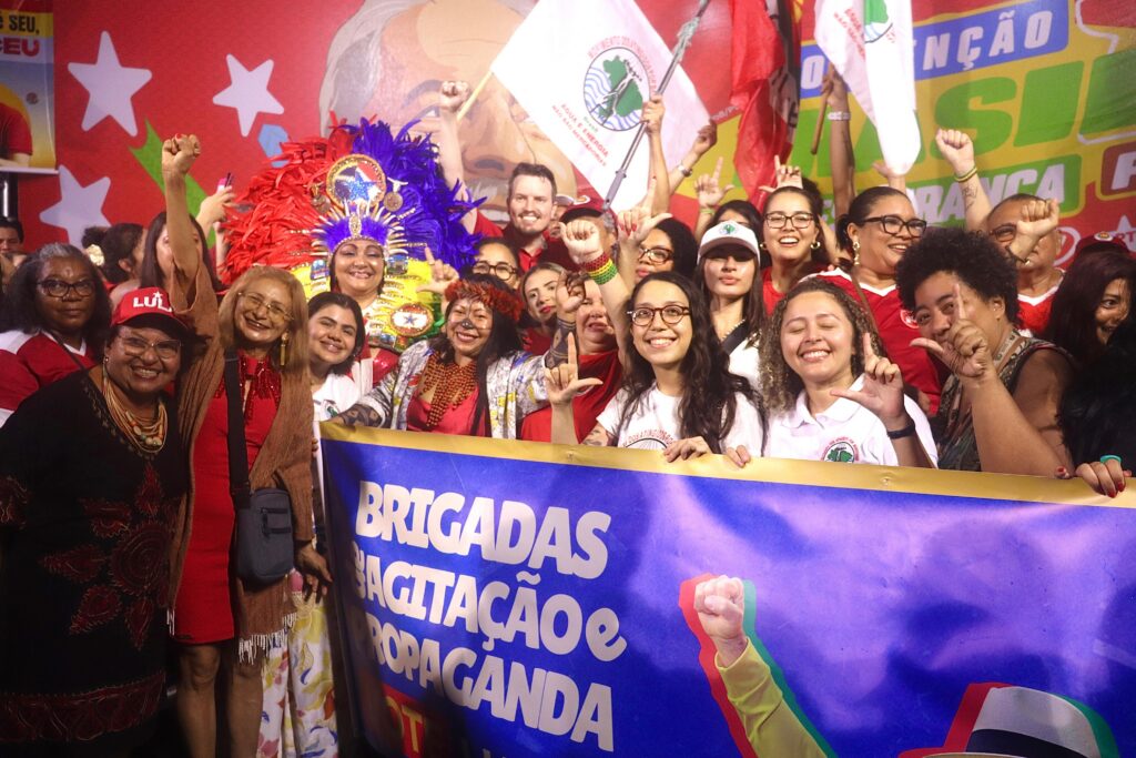 O candidato indicado do PT para compor a chapa majoritária como Vice-Governador, Dirceu Ten Caten e a candidata a Deputada Federal, Alessandra Korap, ao lado de militantes do MAB Amazônia, segurando a bandeira das Brigadas de Agitação e Propaganda, símbolo da mobilização popular em defesa da reeleição do presidente Lula. Foto: Jordana Ayres / MAB Amazônia