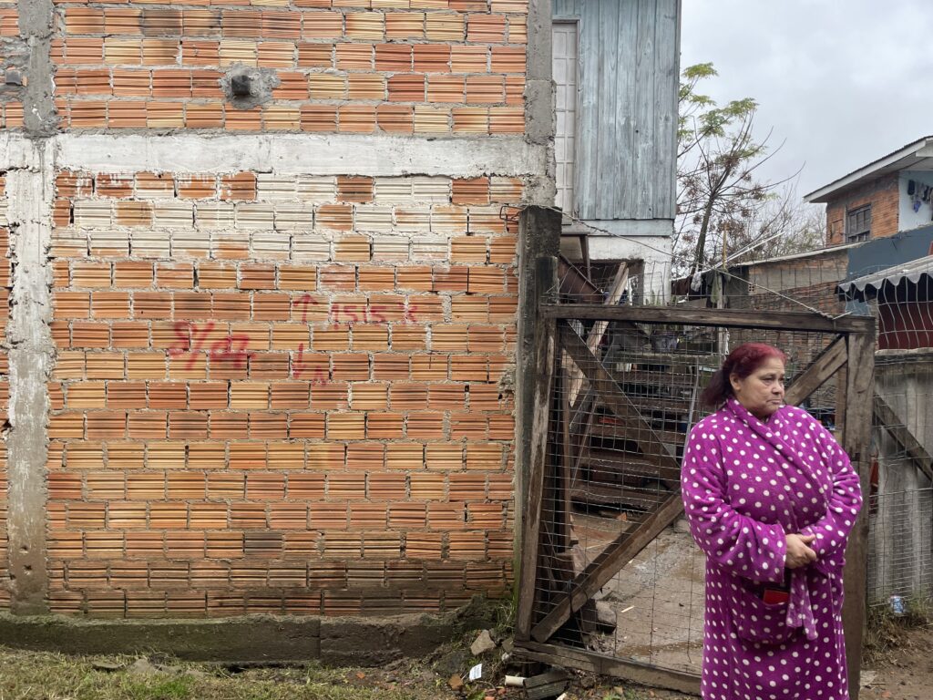 Giane ao lado de sua casa, com data de demolição marcada para 8 de julho de 2026. Foto: Nico Kûara Costamilan / MAB
