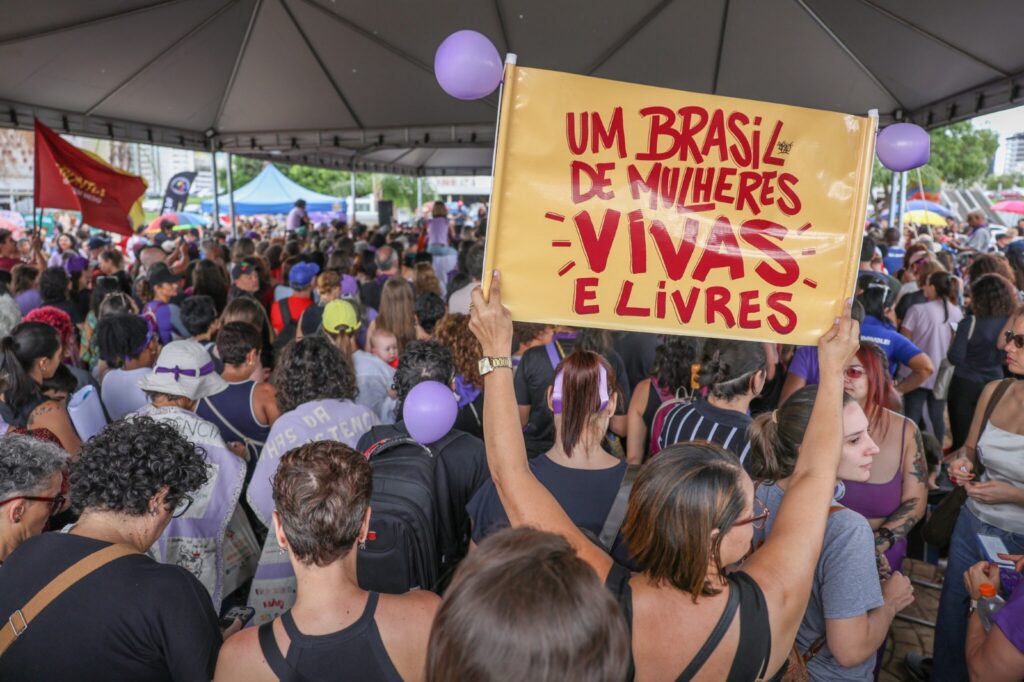 Mulheres reunidas em mobilização nas ruas. Uam delas segura um cartaz com os dizeres "Um Brasil de mulheres vivas e livres". Foto: Marcelo Camargo / Agência Brasil